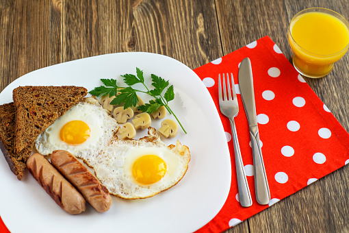 Fried eggs with sausage, marinade mushrooms and rye bread served on a plate on  napkin. Breakfast on the wooden background.