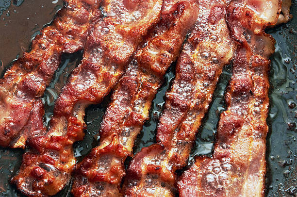 Bacon slice being cooked in frying pan Bacon slice being cooked in frying pan. Close up. cooked bacon slice stock pictures, royalty-free photos & images