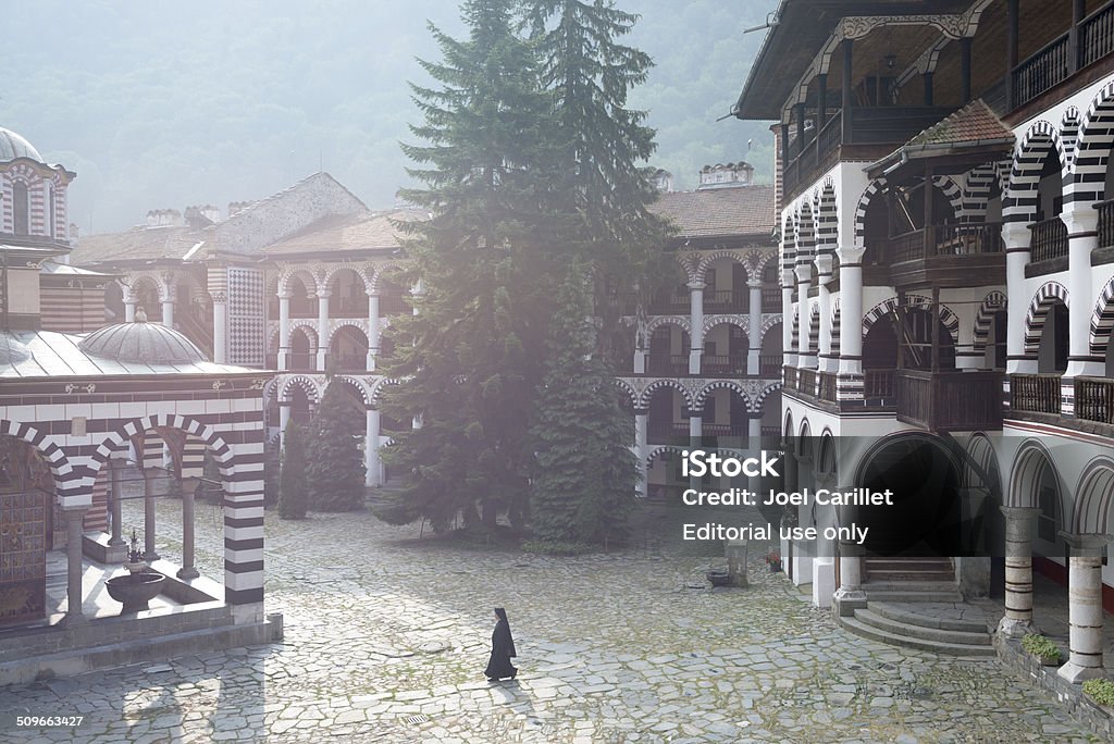 Early morning at Rila Monastery in Bulgaria Rila, Bulgaria - August 25, 2013: A monk in early morning walks in the courtyard of Rila Monastery. The largest and most famous Eastern Orthodox monastery in Bulgaria, it is situated in the southwestern Rila Mountains, 117 km (73 mi) south of the capital Sofia at an elevation of 1,147 m (3,763 ft) above sea level.  It was founded in the 10th century. Bulgaria Stock Photo