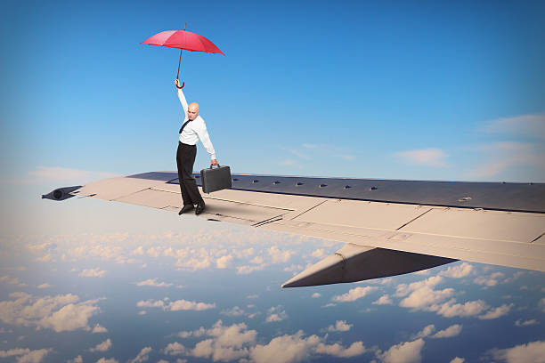 Hazard on the wing. Passenger or pilot with umbrella ballancing on airliner wing. Travel insurance concept. Funny situation from travel. jump jet stock pictures, royalty-free photos & images