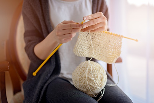 Close up on woman's hands knitting. Sitting on old armchair near window