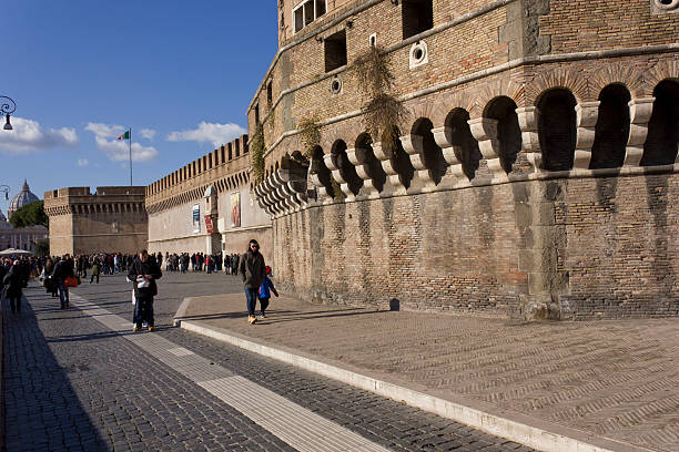 Rome, Italy - December 31, 2014: People walking on Lungotevere Castello in Rome, with the Castle on the side and the Dome of Saint Peter in the backside