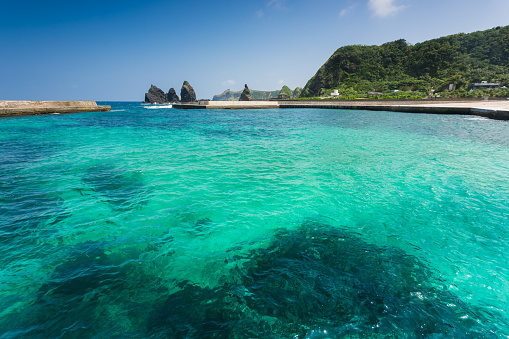 Small remote white beach island with lush green trees in light blue ocean and dramatic sky, Palawan, Philippines