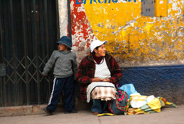 Puno, Peru - April 18, 2010:  A woman and child on a sidewalk selling tortillas against a vibrant yellow wall background.