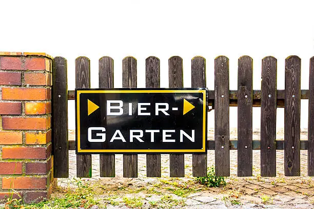 Original german wooden beergarden gate with a typical metal sign. The gate is attached to a masoned post, on the pavement are weeds. Isolated on white.