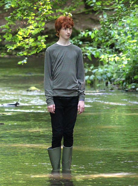 Boy Wading In Shallow River With Green 