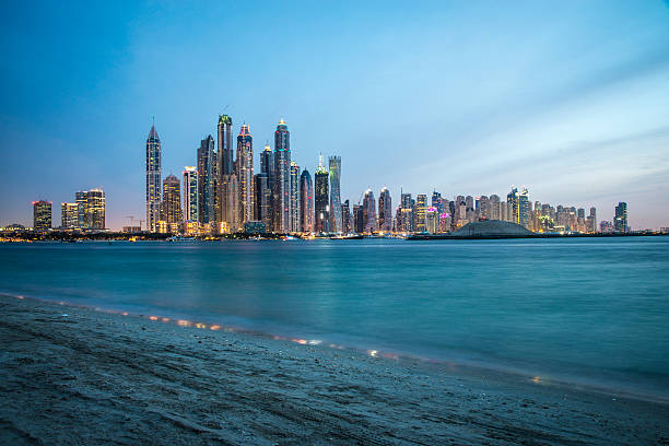 Dubai Marina at Dusk Shot of Dubai marina at dusk, shot from palm Jumeirah. Buildings and sky are illuminated with city lights of different colors. Some boats are seen in front in the sea. A lot of copy space to put your text in. dubai marina panorama stock pictures, royalty-free photos & images