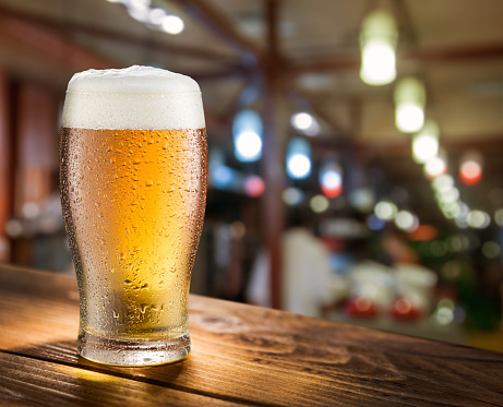 Glass of light beer on the glass bar counter.