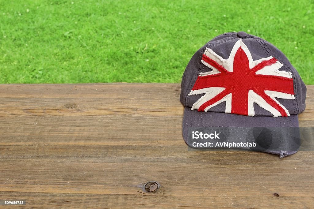 Baseball cap with British flag on wooden table Baseball cap with British flag on wooden table. Lawn in background. Backgrounds Stock Photo