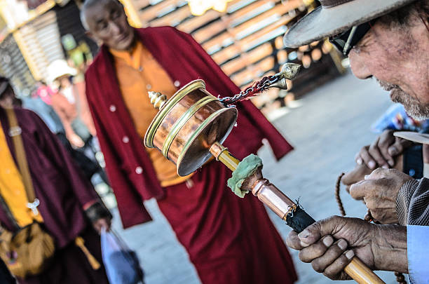 Leh ,India - May 18 , 2019 : An unidentified elderly woman turns a prayer wheel with her hands at the Shey Palace.Prayer wheels are cylindrical wheels on a rotating shaft made of metal, wood, leather on May 18 . 2019.
