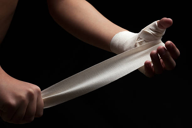 Ready for fight. Beautiful and fit female fighter getting prepared for the fight or training, wrapping her hands with bandage tape against dark background. crossfit girl stock pictures, royalty-free photos & images