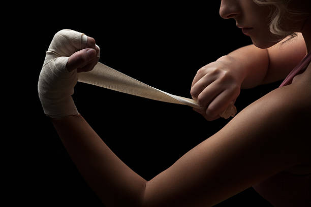 Ready for fight. Beautiful and fit female fighter getting prepared for the fight or training, wrapping her hands with bandage tape against dark background. crossfit girl stock pictures, royalty-free photos & images