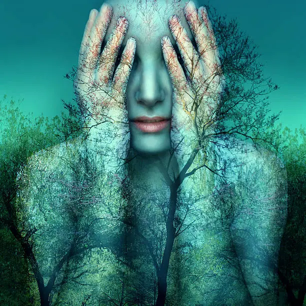 Surreal and artistic image of a girl who covers her eyes with her hands on a background of trees and sky