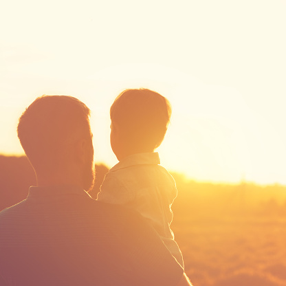 Silhouette of the father and his son during sunset.They are spending day together outdoors in the nature.