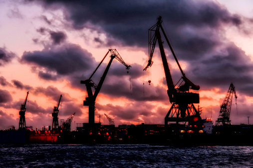 A shipyard with cranes at sunset light with dramatic stormclouds, graphic effect