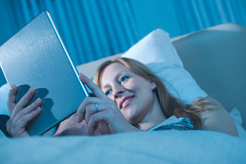 A woman looking reading on digital tablet at night