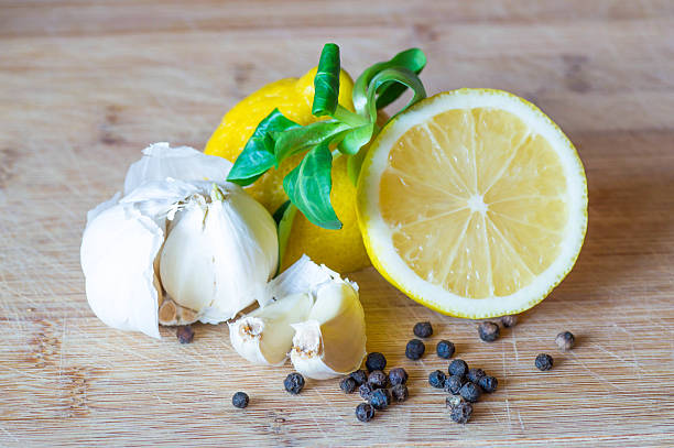 Front view of a halved lemon, salad and garlic with garlic cloved surrounded with black pepper