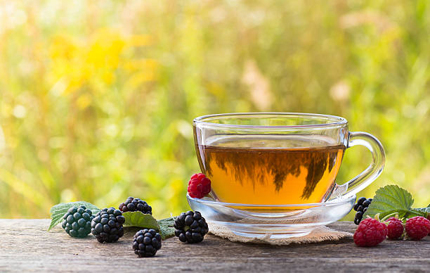 istock Cup of tea with raspberry and blackberry on meadow background 509755449