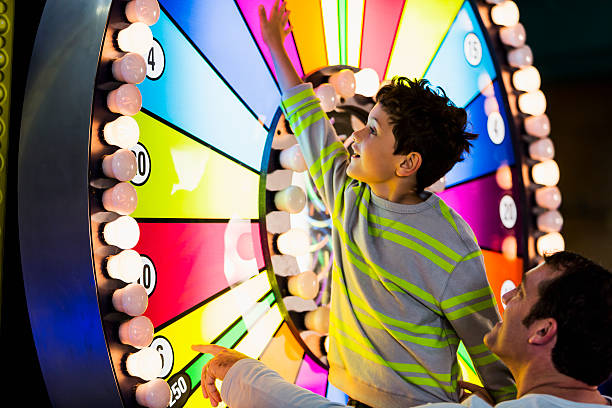 Father and son at an amusement arcade Little boy (5 years, mixed race, Hispanic / Caucasian) with father, spinning a colorful, illuminated wheel at an amusement arcade. arcade photos stock pictures, royalty-free photos & images