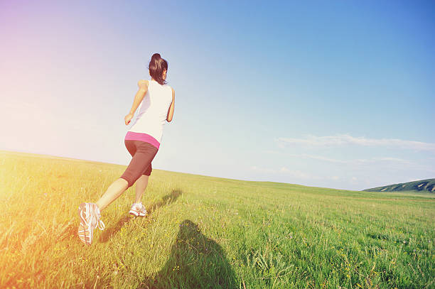 Runner athlete  running on sunrise/sunset grass field. woman fitness jogging workout wellness concept.