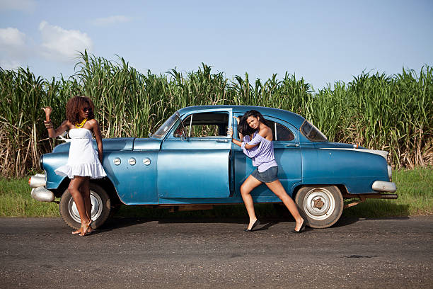 Two women hitchhiking beside their old fashioned car on the road, alone.