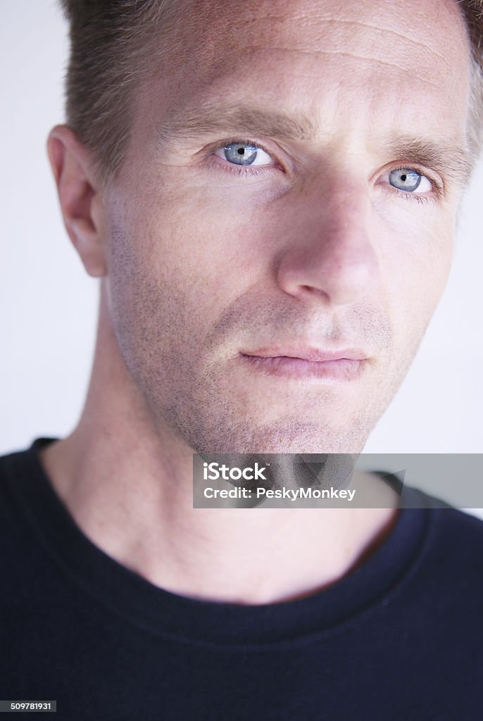 Serious Young Adult Man in Dark T-Shirt Looking at Camera Serious young adult man with blue eyes in dark t-shirt looking at the camera in a close-up portrait Adult Stock Photo