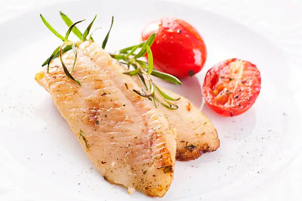 Fried fish fillet with tomatoes as closeup on a white plate