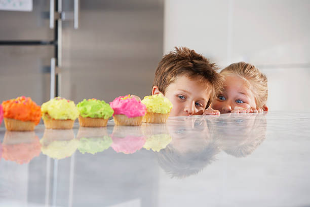 Siblings Peeking Over Counter At Row Of Cupcakes Young girl and boy peeking over counter at row of cupcakes kid peaking over counter stock pictures, royalty-free photos & images