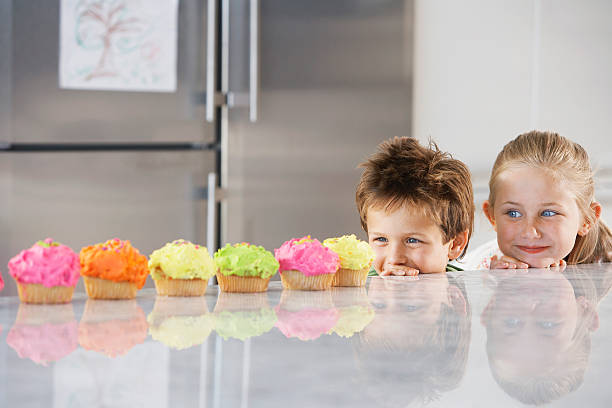 Siblings Peeking Over Counter At Row Of Cupcakes Young girl and boy peeking over counter at row of cupcakes kid peaking over counter stock pictures, royalty-free photos & images