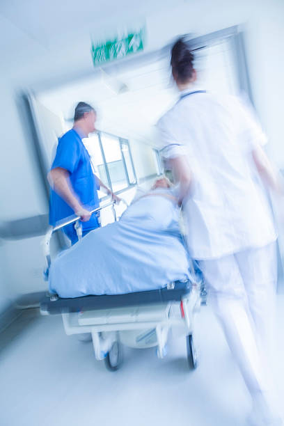 Motion Blur Stretcher Gurney Patient Hospital Emergency A motion blurred photograph of a senior female patient on stretcher or gurney being pushed at speed through a hospital corridor by doctors & nurses to an emergency room hospital emergency sign stock pictures, royalty-free photos & images