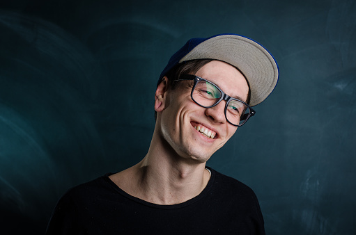 young man wearing glasses and a cap on dark background