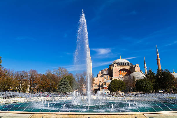 Water fountain in blue sky. Seen in the background is Hagia Sofia (Holly Wisdom) basilica in Istanbul Turkey. It was built as a church, later was converted into a mosque, and now is a museum.