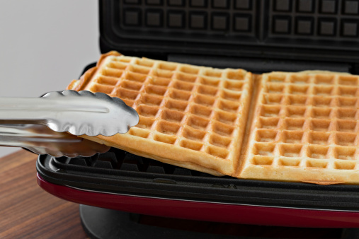 An extreme close up shot of a cook removing waffles from a waffle maker.