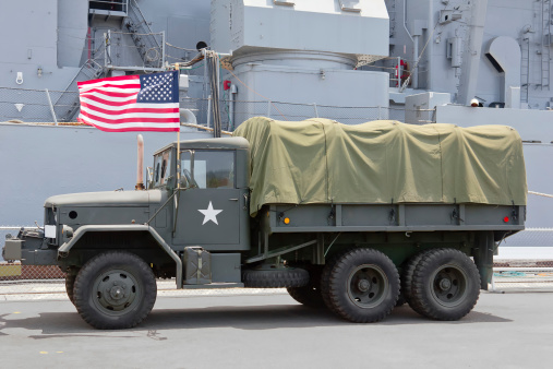 Navy ship sits in the background behind a military truck.
