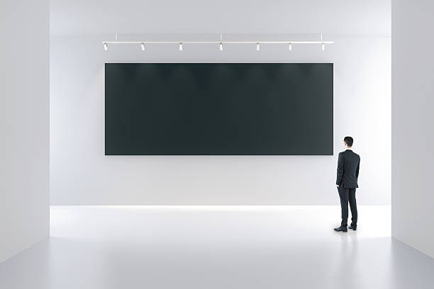 istock Blank black poster and businessman in white empty room 509806090