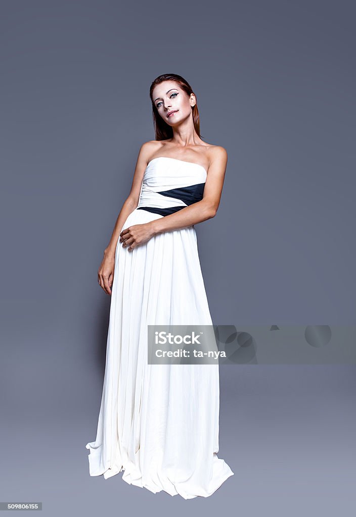 Beautiful woman in stylish white luxury dress Attractive woman with perfect professional make-up and simple hairstyle, wearing beautiful white dress. Fashion model studio portrait on dark background. Full length body. One Woman Only Stock Photo