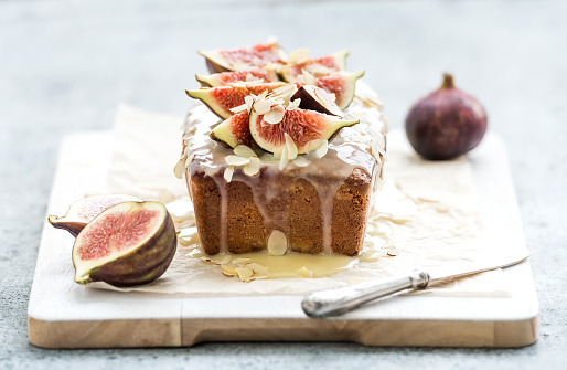 Loaf cake with figs, almond and white chocolate on white serving board over grunge background, selective focus