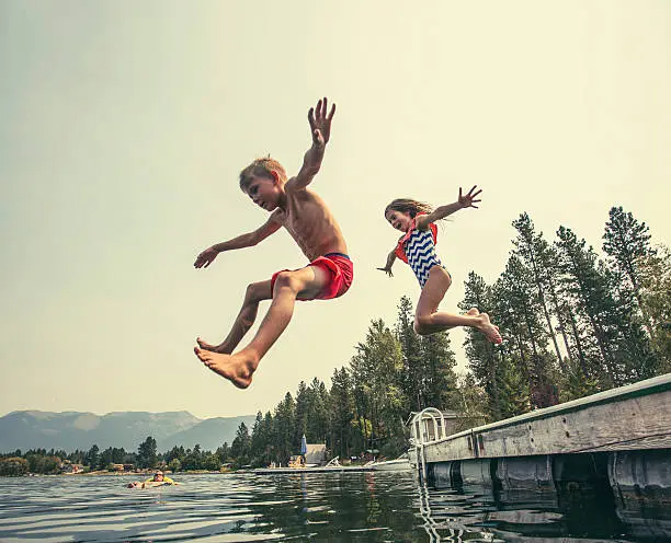 A little boy and little girl jumping off the dock into a beautiful mountain lake. Having fun on a summer vacation