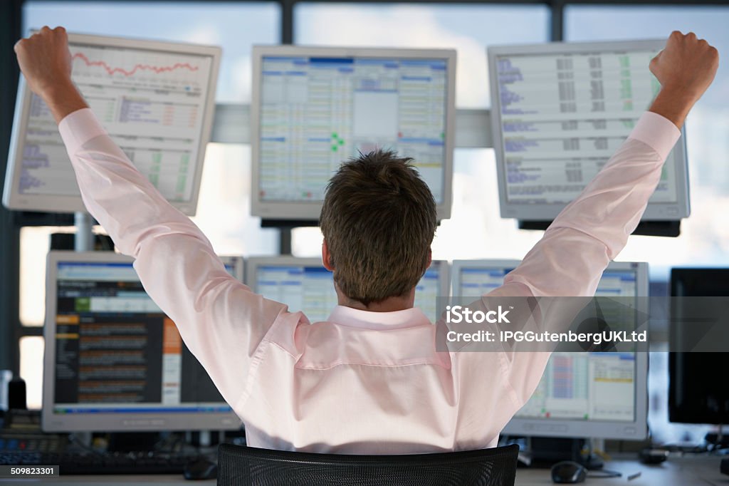 Stock Trader Watching Computer Screens With Hands Raised Rear view of stock trader with hands raised looking at multiple computer screens Adult Stock Photo