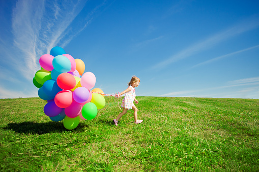 Happy little girl holding colorful balloons. Child playing on a green meadow. Smiling  kid.