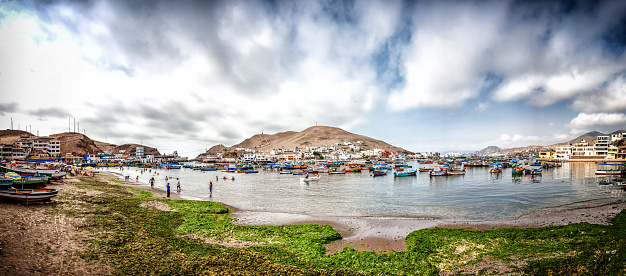 Pucusana, Peru - January 12, 2015: Peruvian coastal village at Pucusana. Boats are at anchor in the harbour while people are pictured bathing at the water's edge