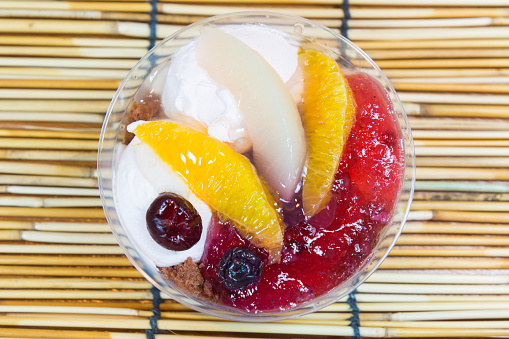 Ice cream and fruits in the plastic bowl on bamboo background.