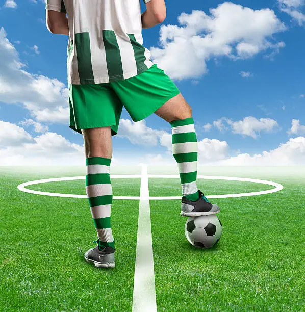 Football player with a ball between his legs standing on the  football ground