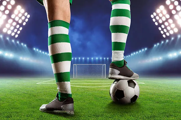 Football player legs with a ball standing on the football ground