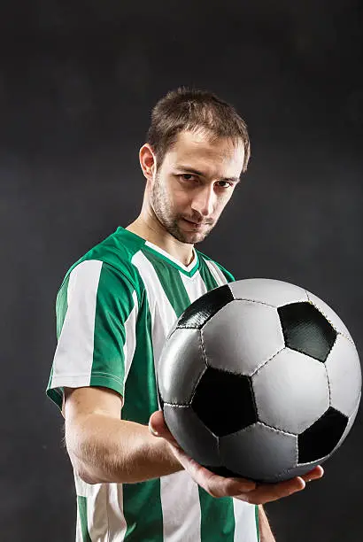 Football-player holding a ball over black background