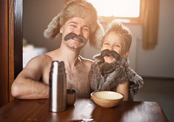Portrait of a stereotypical eastern european polish or russian man and his son laughing. The man is aged 35-40 years and is wearing big moustache and fur hat. Also the little son wears mustache.