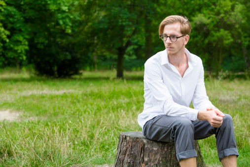 young man in a white shirt sitting on a tree stump