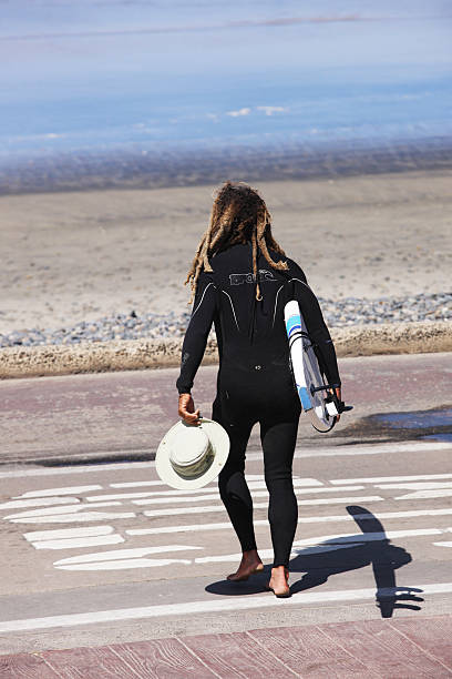 Wetsuit Surfer Athlete Carrying Surfboard La Jolla, California, USA - June 19, 2014: Veteran surfer carries his board and hat to the beach after stretching and warming up along the boardwalk. He's using an 8' Wavestorm surfboard with a skived 3-D pad for good foot traction. La Jolla offers a number of beaches with good beach breaks and a variety of wave types for surfers. mavericks california stock pictures, royalty-free photos & images