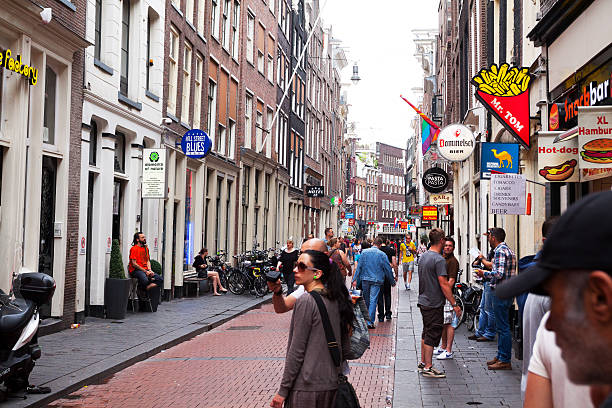 People in Warmoesstraat Amsterdam, The Netherlands - June 9, 2014: Summer shot of people and tourists walking in street Warmoesstraat in summer. Popular street in Wallen with many bars and coffee shops. Some people are sitting outside in front of buildings. wellen stock pictures, royalty-free photos & images