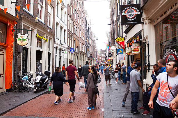 Walking along street Warmoesstraat in Amsterdam Amsterdam, The Netherlands - June 9, 2014: View along street Warmoesstraat in Amsterdam in summer. People and tourists are walking and doing sight seeing. In street are many bars and coffee shops. wellen stock pictures, royalty-free photos & images